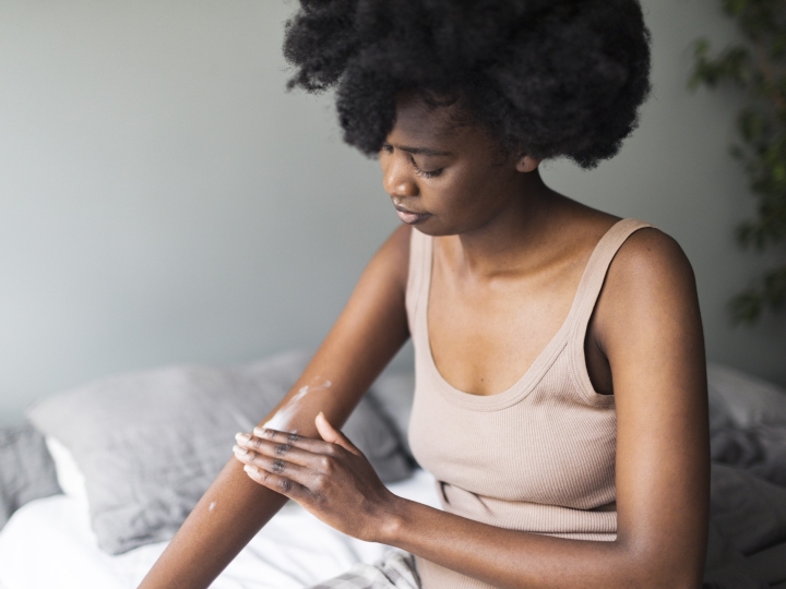 Black woman applying body lotion